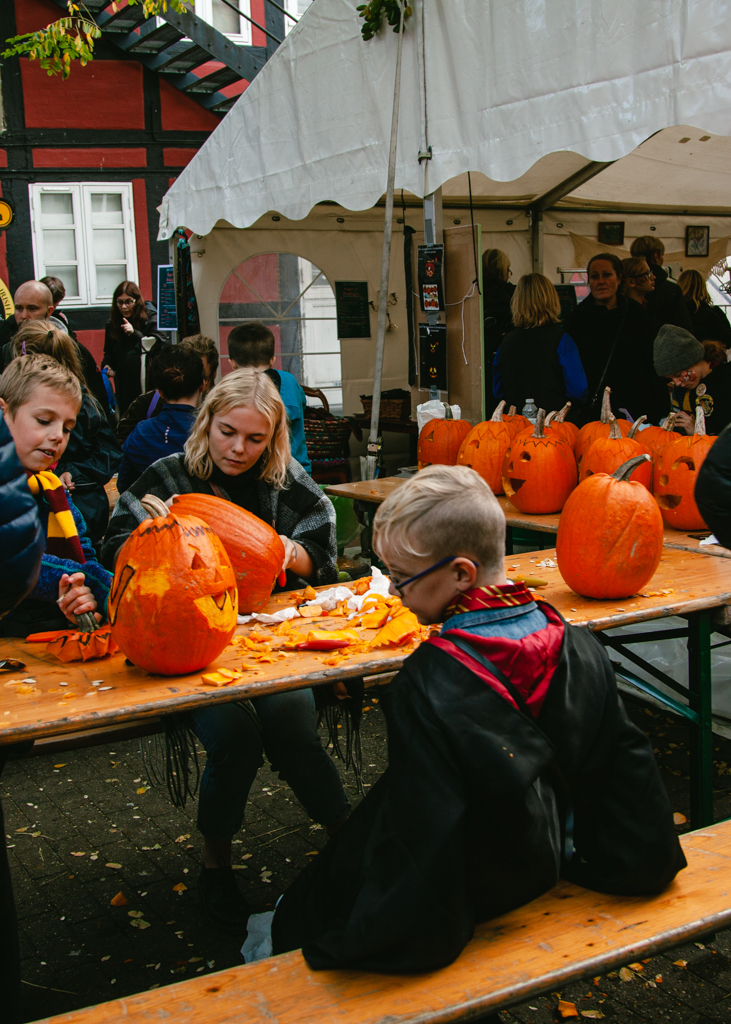 Two young children and an adult carving pumpkins at a community table.
