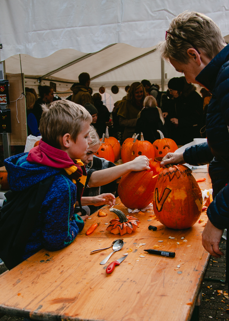 A young child and an adult carving a pumpkin at a community table.