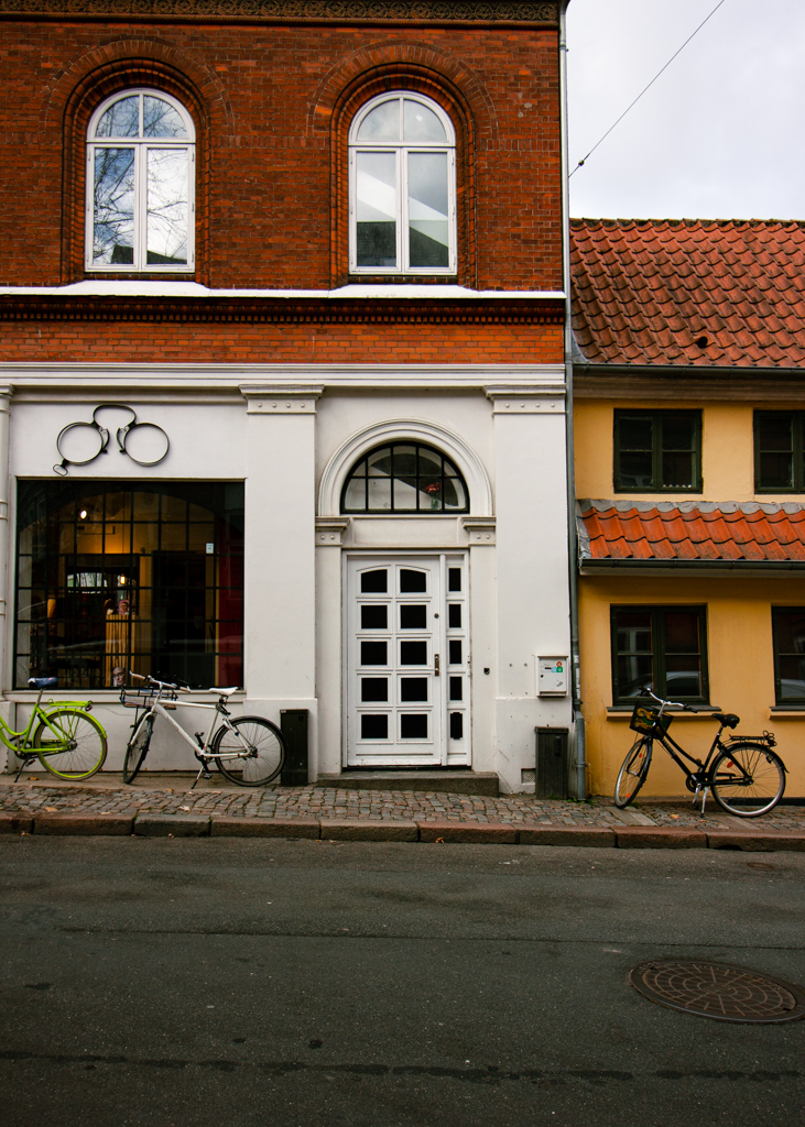 The store front of a bike shop, with three bikes parked in front of it.