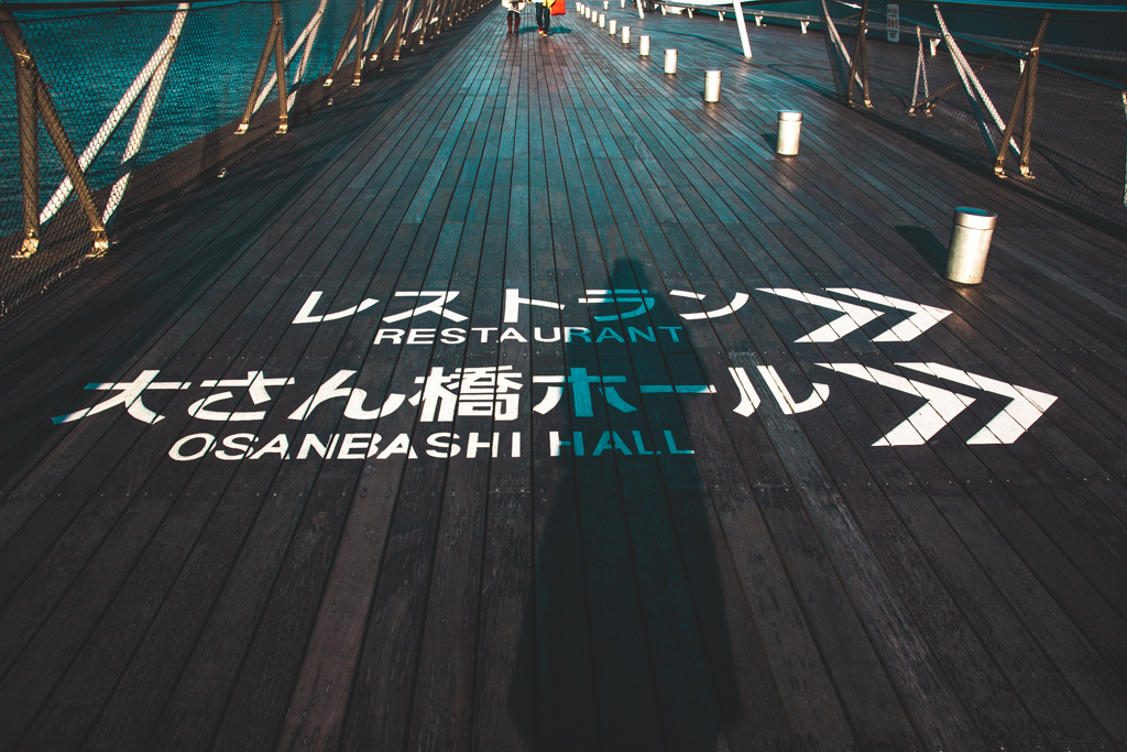 Wooden paneled floor on the port in Yokohama with painted directory pointing to the Restaurant and Osanbashi Hall in the right direction.
